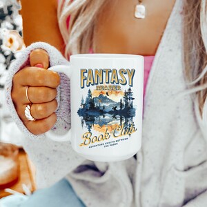 Może przedstawiać: Biały kubek ceramiczny z niebiesko-żółtą ilustracją leśnej sceny i tekstem "Fantasy Reader Book Club Adventure awaits between the pages".
