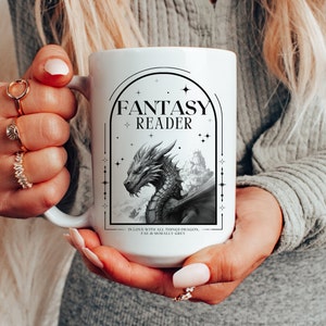 May include: White ceramic mug with a black and white illustration of a dragon and the text "Fantasy Reader" in a black arch. The text below the arch reads "In love with all things dragon, fae & morally grey."