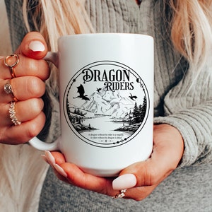 May include: White ceramic mug with a black and white illustration of a dragon, mountains, and a lake. The text "Dragon Riders" is printed in a circle around the illustration. The text "A dragon without a rider is a tragedy. A rider without a dragon is dead." is printed below the circle.