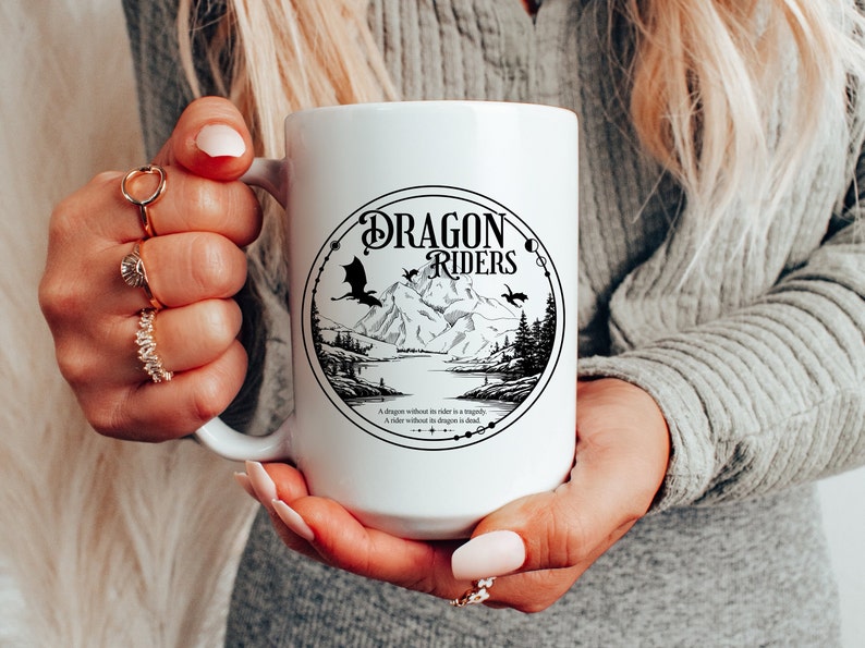 May include: White ceramic mug with a black and white illustration of a dragon, mountains, and a lake. The text "Dragon Riders" is printed in a circle around the illustration. The text "A dragon without a rider is a tragedy. A rider without a dragon is dead." is printed below the circle.