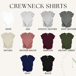 Op de afbeelding: Een selectie van crewneck t-shirts in verschillende kleuren, waaronder wit, as, atletiek heather, donker heather, naturel, heather mauve, maroon, militaire groen, marineblauw en zwart.