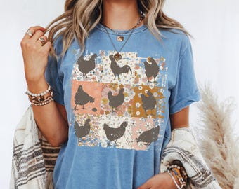 May include: A blue t-shirt with a patchwork design featuring a rooster and chickens. The design is in a vintage style with floral patterns and a distressed look.