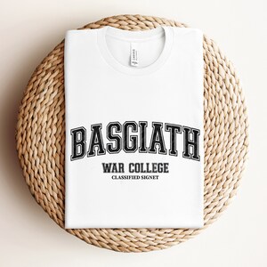 Op de afbeelding: Wit T-shirt met een zwarte grafische print met de tekst "Basgiath War College Classified Signet".