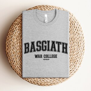 Op de afbeelding: Grijs T-shirt met zwarte tekst die "Basgiath War College Siphon" luidt.
