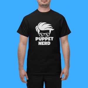 May include: Black t-shirt with a white graphic of a person with blonde hair wearing sunglasses and the text "Puppet Nerd".