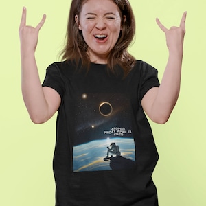 May include: A black t-shirt with a graphic of an astronaut sitting on a cliff overlooking Earth. The graphic includes a solar eclipse and the text "APOPHIS FRIDAY APRIL 13 2029".