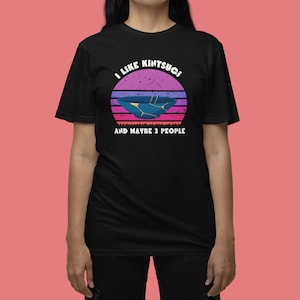May include: Black t-shirt with a graphic of a kintsugi bowl set against a sunset backdrop. The text says "I like kintsugi and maybe 3 people". The design uses blue, purple, and pink hues.