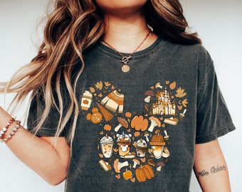 May include: A dark gray t-shirt with a Mickey Mouse silhouette made up of fall-themed images, including pumpkins, leaves, coffee cups, and a castle.