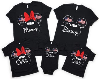 May include: Black t-shirts with a patriotic design featuring a red bow, American flags, and the text "USA 1776 * 2026". The shirts are customized with the words "Mommy", "Daddy", "Olivia", and "Oliver".