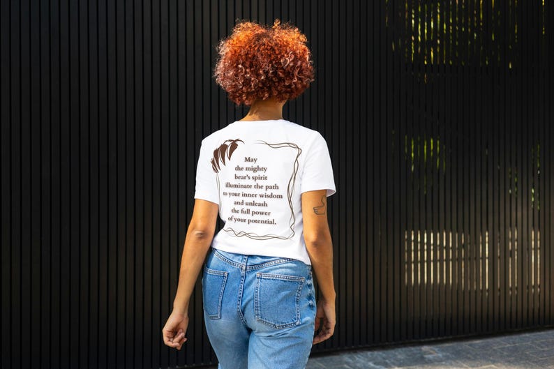 May include: White t-shirt with a brown graphic print of a bear and text that reads "May the mighty bear's spirit illuminate the path to your inner wisdom and unleash the full power of your potential."