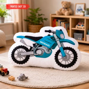 Puede incluir: Un coj&iacute;n blanco con forma de motocicleta con un dise&ntilde;o turquesa y negro. El coj&iacute;n tiene el nombre "MICHAEL" impreso en el lateral. El texto "PRINTED (NOT 3D)" est&aacute; impreso en rojo en la parte superior izquierda.