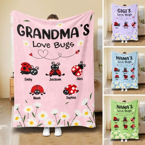 Op de afbeelding: Een roze fleece deken met een witte madeliefjesrand en een gepersonaliseerd bericht dat "Grandma's Love Bugs" zegt. De deken heeft vijf lieveheersbeestjes met namen eronder geschreven.