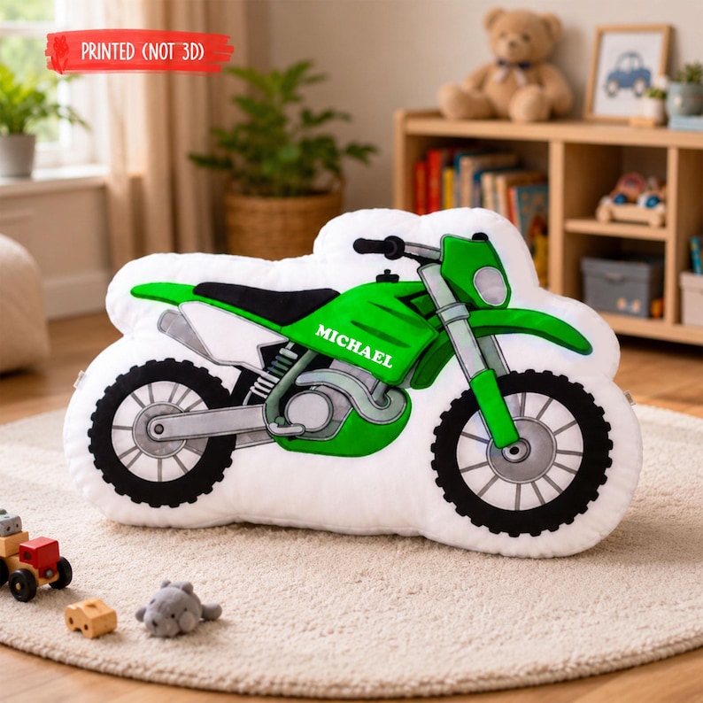 Puede incluir: Un coj&iacute;n blanco de felpa con forma de motocicleta con detalles verdes y negros. El coj&iacute;n tiene un marco verde, neum&aacute;ticos negros y el nombre "MICHAEL" impreso en el lateral. El texto "PRINTED (NOT 3D)" est&aacute; impreso en una pancarta roja.