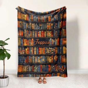 May include: A soft, plush fleece blanket featuring a bookshelf design with colorful books and autumn leaves. The name "Jessica" is printed in a cursive font on the blanket.