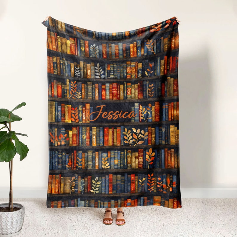 May include: A soft, plush fleece blanket featuring a bookshelf design with colorful books and autumn leaves. The name "Jessica" is printed in a cursive font on the blanket.