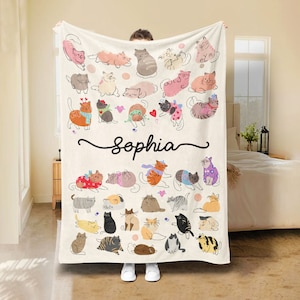 May include: A cream-colored fleece blanket with a personalized name "Sophia" in black cursive script. The blanket features a colorful pattern of various cats in different poses and colors.