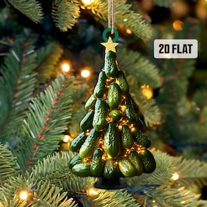 May include: A novelty Christmas tree ornament made of green pickle-shaped decorations, illuminated with small lights. The ornament is suspended by a twine string and a green ring, topped with a gold star. The text "2D FLAT" is visible.