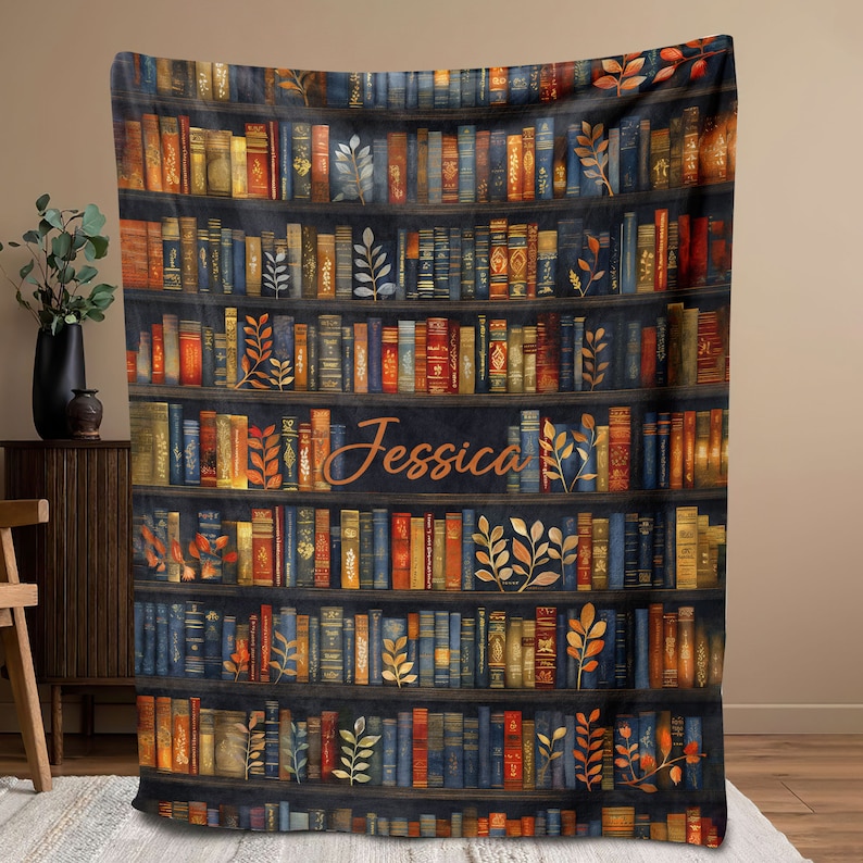 May include: A navy blue fleece blanket with a bookshelf design featuring rows of colorful books and gold leaf accents. The name "Jessica" is written in a cursive font on the blanket.
