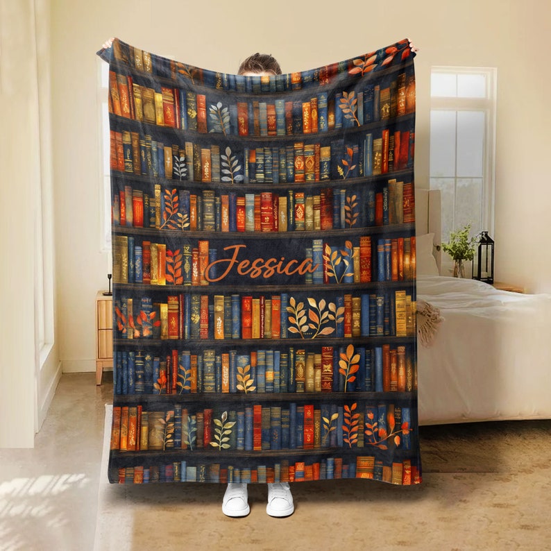 May include: A personalized fleece blanket with a bookshelf design featuring a variety of colorful books and gold leaf accents. The name "Jessica" is written in a cursive font on the blanket.
