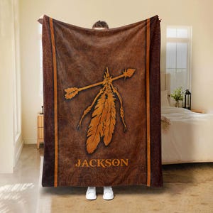 May include: Brown fleece blanket with a Native American inspired design featuring a feather and arrow with the name "JACKSON" printed below.