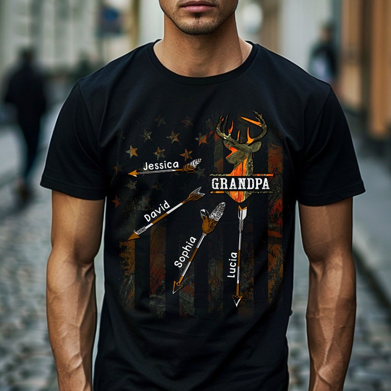 May include: Black t-shirt with a camouflage pattern and an American flag design. The design features a deer head with antlers and arrows pointing to the names Jessica, David, Sophia, and Lucia. The text "GRANDPA" is written above the deer head.