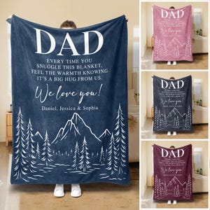 May include: A blue fleece blanket with a white mountain scene and the text "DAD EVERY TIME YOU SNUGGLE THIS BLANKET. FEEL THE WARMTH KNOWING IT'S A BIG HUG FROM US. We love you! Daniel, Jessica & Sophia"