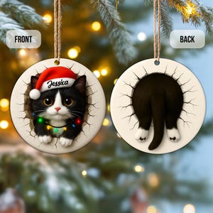 May include: A round Christmas ornament featuring a black and white cat wearing a Santa hat and a string of colorful lights. The cat's name, "Jessica," is printed on the hat. The back of the ornament shows the cat's rear end.