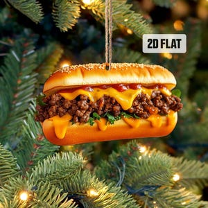 May include: A 2D flat ornament shaped like a cheeseburger with a beef patty, cheese, lettuce, and tomato. The ornament is hanging from a Christmas tree.