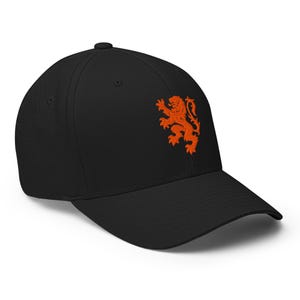 May include: A black baseball cap featuring an embroidered orange lion emblem on the front panel. The cap has a structured crown, a curved brim, and a button at the top center. The design is centered on the front of the hat.