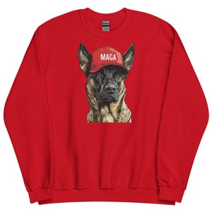 Peut inclure: Un sweat-shirt rouge avec un graphisme d'un berger allemand portant une casquette rouge avec le mot "MAGA" en blanc. Le visage du chien est détaillé avec des poils et une expression réalistes.