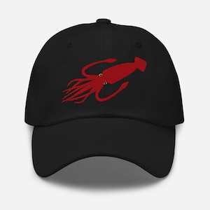 Könnte beinhalten: Schwarze Baseballkappe mit einem roten, gestickten Tintenfisch-Design. Der Tintenfisch hat detaillierte Tentakel und zwei kleine gelbe Augen. Die Kappe besteht aus einem weichen Stoff und hat einen gebogenen Schirm.