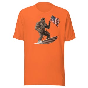 Patriotic Bigfoot Shirt, Surfing Bigfoot Holding American Flag Short Sleeve Crewneck Tshirt, Funny Sasquatch Tee, Multiple Colors