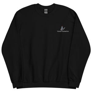 Könnte beinhalten: Schwarzes Sweatshirt mit einem gestickten Design eines Ritters mit Schwert und dem Text "'Tis but a scratch!" in Weiß. Das Sweatshirt mit Rundhalsausschnitt ist aus einem weichen Material gefertigt.