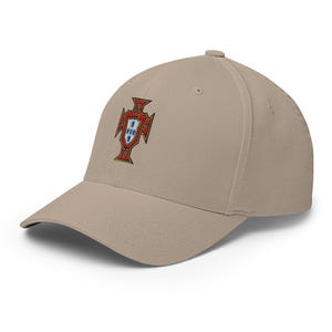 May include: A tan baseball cap featuring an embroidered emblem of the Portuguese coat of arms. The emblem is red, gold, and blue. The cap has a curved brim and a structured crown.
