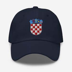 Puede incluir: Gorra de béisbol azul marino con un escudo de armas croata bordado. El emblema incluye un escudo a cuadros rojo y blanco, coronado por una corona en azul, amarillo y rojo. Un accesorio elegante para los fans de Croacia.