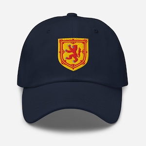May include: A navy blue baseball cap with an embroidered emblem. The emblem is a yellow shield with a red lion rampant, blue claws and tongue, and a red border. A classic, adjustable hat.