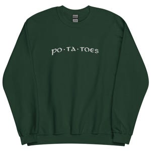 Puede incluir: Sudadera verde oscuro con la palabra "po.ta.toes" en letras blancas estilizadas en el pecho. La sudadera tiene cuello redondo y mangas largas. La etiqueta de la marca Gildan es visible.