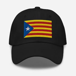 Puede incluir: Gorra de béisbol negra con un diseño de bandera bordada. La bandera tiene rayas horizontales amarillas y rojas, un triángulo azul y una estrella blanca.