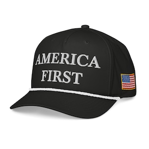 May include: Black baseball cap with the embroidered text "AMERICA FIRST" in white. The cap features a white rope detail along the brim and a small American flag patch on the side.