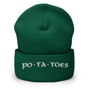 Puede incluir: Un gorro verde oscuro con la palabra "po.ta.toes" bordada en blanco. El gorro es de estilo tejido, con un borde doblado y una parte superior redondeada. El texto está centrado en el borde.