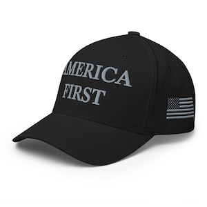 May include: Black baseball cap with the text "AMERICA FIRST" embroidered in gray on the front. The American flag is embroidered on the side. The cap has a curved brim and a structured fit.