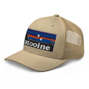 May include: A tan trucker cap with a mesh back and a curved peak. The front displays an embroidered patch with the word "tatooine" in white, and a rectangular design with blue, orange, and white stripes.