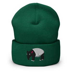 Puede incluir: Un gorro verde oscuro con un borde doblado. El gorro presenta una imagen bordada de un tapir con cabeza y patas negras, cuerpo blanco y oreja rosa.