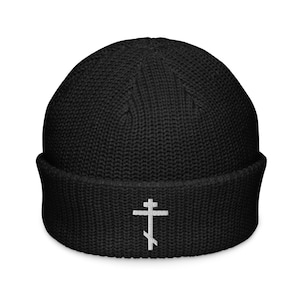 May include: Black beanie with a white Eastern Orthodox cross embroidered on the front. The hat is made of a ribbed knit fabric and has a folded brim. The cross is a traditional symbol of Christianity.