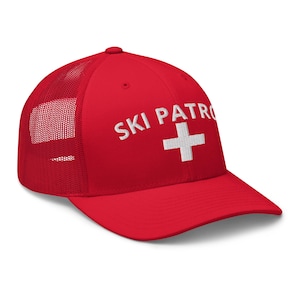 May include: A red trucker cap with a white mesh back. The front of the cap has the text "SKI PATROL" above a white cross. This cap is suitable for outdoor activities and offers sun protection.