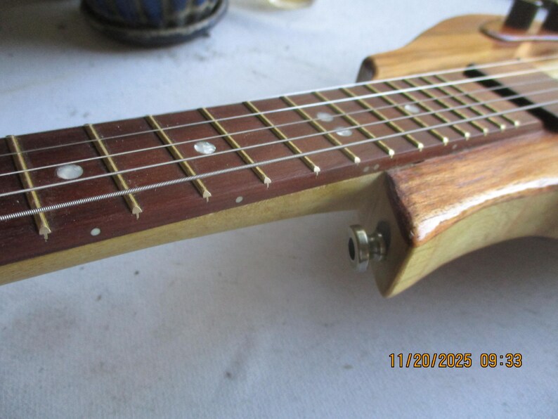 May include: Close-up of a wooden stringed instrument's fretboard. The fretboard is a dark brown colour with white dot inlays. The strings are silver and the frets are gold. The instrument's body is a light brown colour.