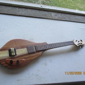 May include: A handcrafted electric guitar with a distinctive body shape. It has a light wood central section, a dark fretboard, and a gold-coloured bridge. The headstock is intricately designed. The guitar is made of wood.