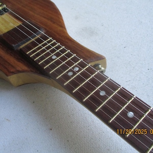 May include: Close-up of a wooden electric guitar. The instrument has a dark brown body and neck with a lighter wood section. The fretboard has inlaid white dots. The strings are visible, and the date 11/20/2025 09:33 is in the bottom right corner.