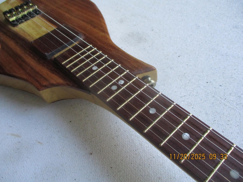 May include: Close-up of a wooden electric guitar. The instrument has a dark brown body and neck with a lighter wood section. The fretboard has inlaid white dots. The strings are visible, and the date 11/20/2025 09:33 is in the bottom right corner.