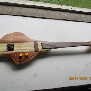 May include: A custom electric guitar with a distinctive body shape. It has a light wood body with darker wood accents, a fretboard, and two gold knobs. The headstock has a natural wood finish. The guitar is approximately 76 cm long.